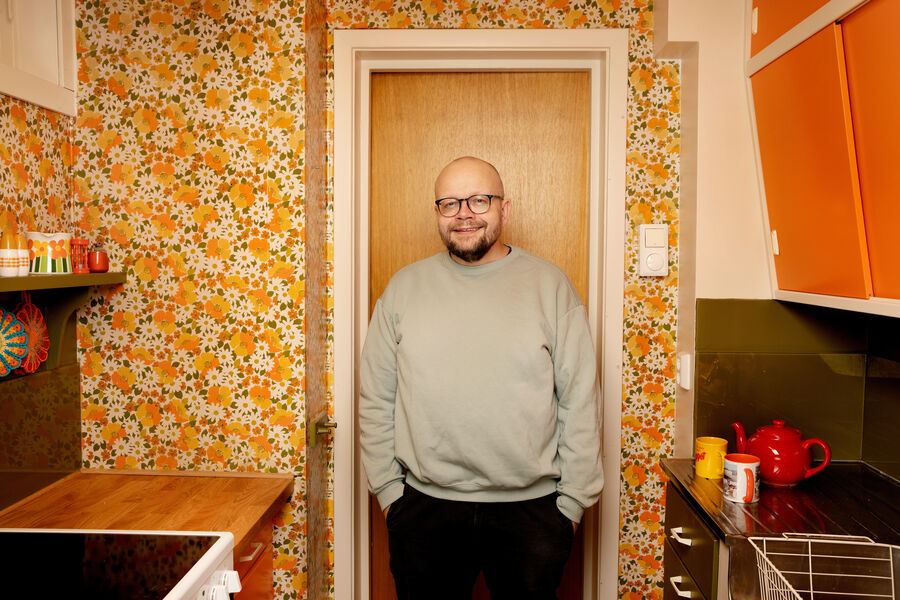 Bilde av forfatter Bjørn Hatterud i et kjøkken med en oransje tapet med blomster-motiv. 