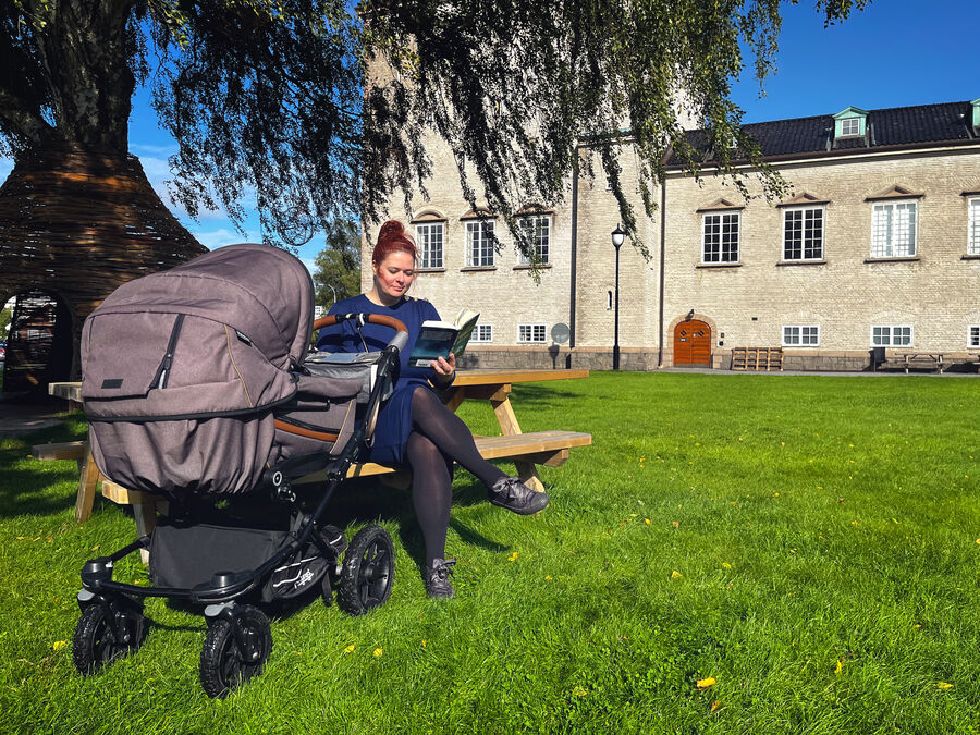 Dame leser bok med barnevogn utenfor Fredrikstad bibliotek 