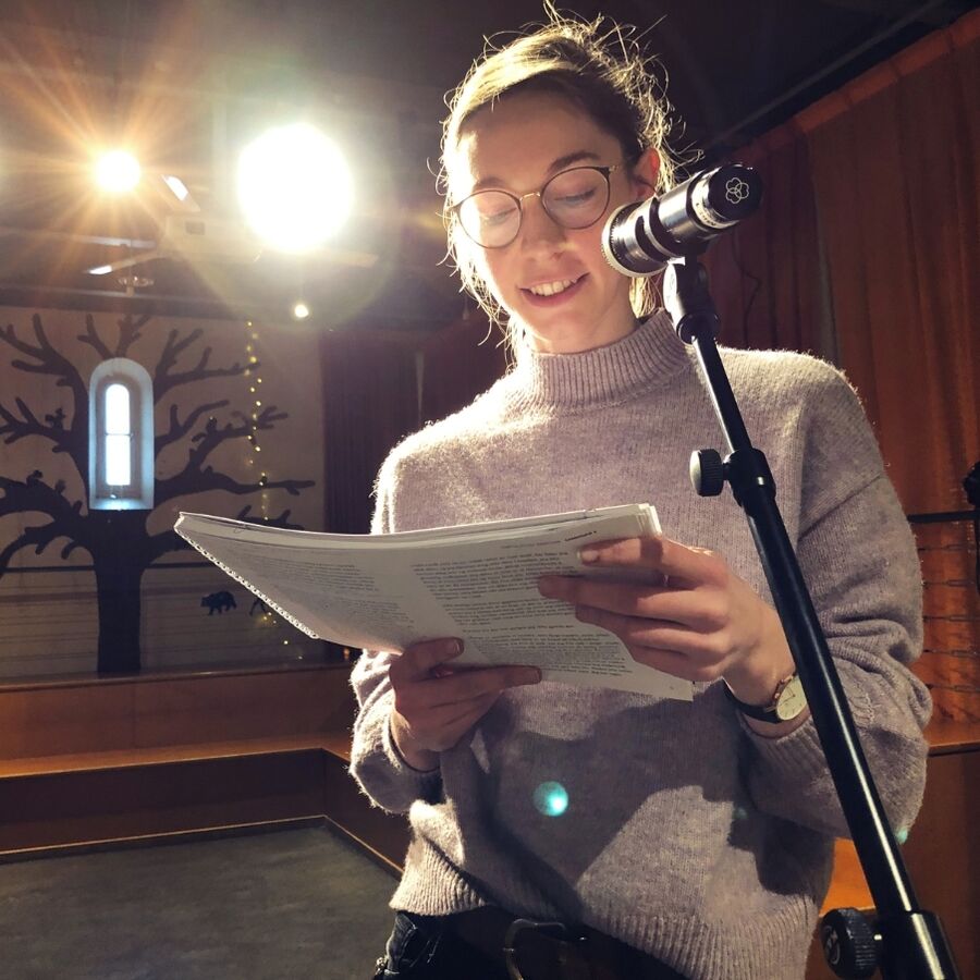Bibliotekar Andrea leser fra en bok i en mikrofon med scenelys i bakgrunnen