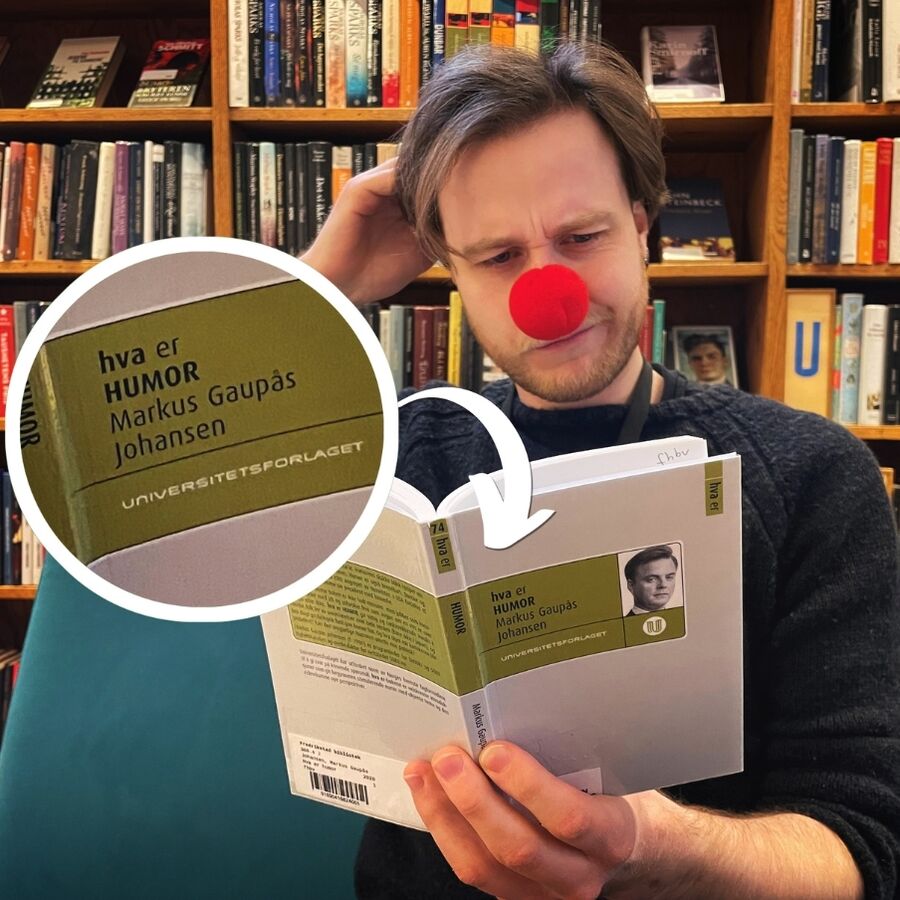 Bibliotekar Thorbjørn leser i boka Hva er humor? av Markus Gaupås Johansen iført klovnenese mens han klør seg i hodet og ser skeptisk ut