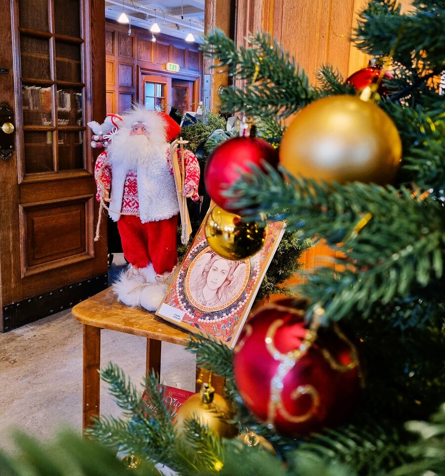 Bilde av et pyntet juletre på biblioteket med en nissedukke i bakgrunnen