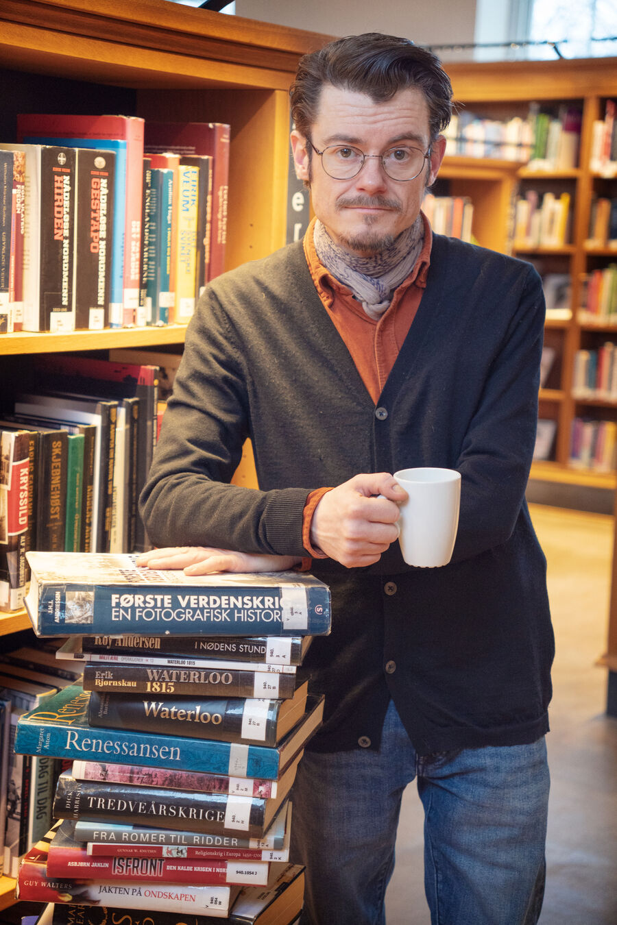 Bilde av bibliotekar Martin som står med kaffekoppen ved siden av en svær stabel med historiebøker