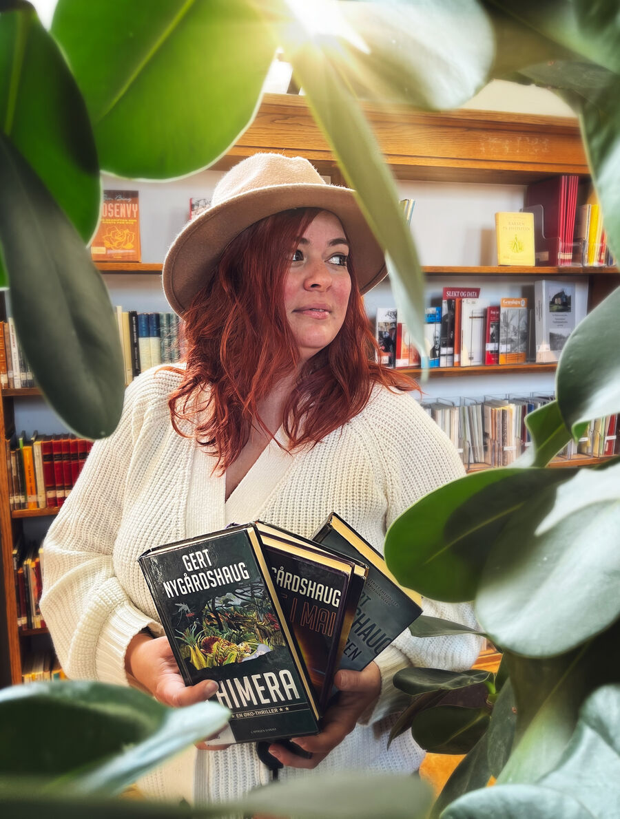 Bilde av formidler Ingrid Rekdal som har på seg en Gert Nygårdshaug-hatt, mens hun holder bøker han har skrevet med planer rundt seg
