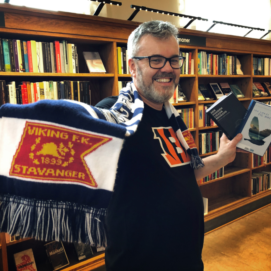 Bilde av bibliotekar Dag Einar som holder bøker fra Stavanger-forfattere og et skjerf med fotballaget Viking  
